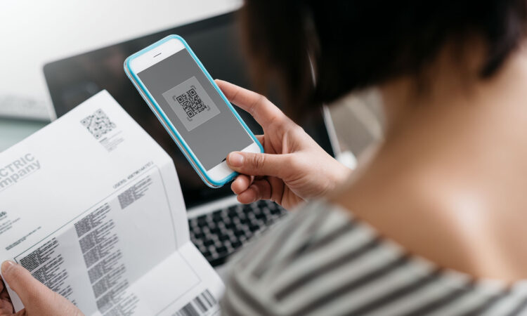 A woman holding her phone and looking down at the phone and a bill she is holding in her other hand