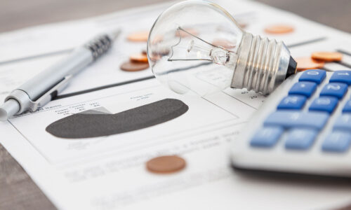 A lightbulb, calculator, pens and some paper with a pie chart on it laid out on a desk