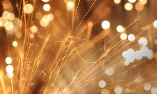 Up close image of sparklers and sparks set to an dark orange slightly blurred background.