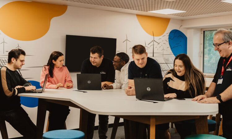 A group of team members from Lumina Energy in the office, at a large table looking at laptops, smiling.