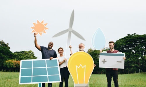Four people in a field holding cut outs of energy icons - solar panel, sun, wind turbine, battery and light bulb